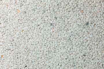 A close-up view of white gravel stones creating a textured and natural background. The small pebbles form an abstract pattern, commonly used for landscaping, construction, and decorative purposes