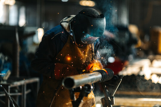 A welder in protective gear works on a metal structure, creating bright sparks and smoke in an industrial workshop. The intense focus and dramatic lighting highlight the craftsmanship and precision of - Powered by Adobe