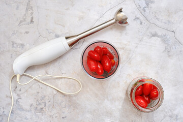 Preparation of fresh cherry tomatoes for a culinary dish using a hand blender in a kitchen setting