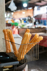 Freshly fried youtiao in a wire basket, ready to serve. Close-up of golden brown savory Asian fried bread snack.