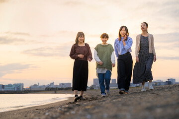 夕暮れの中、寄り添って海沿いを歩く女性4人