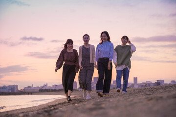 夕暮れの中、寄り添って海沿いを歩く女性4人