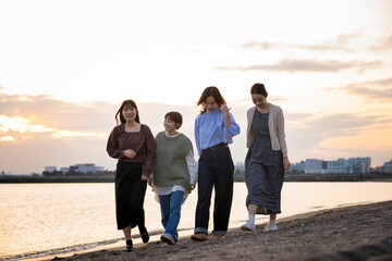 夕暮れの中、寄り添って海沿いを歩く女性4人