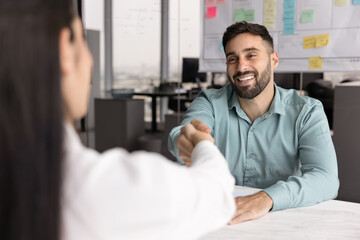 Fototapeta premium Positive handsome young Latin businessman in casual shaking hands with female financial legal advisor, business partner, colleague, thanking for meeting, consultation, closing deal