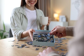Couple with puzzle pieces at wooden table indoors, closeup