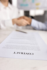 Close up of paper contract on office table with two business partners shaking hands in blurred...