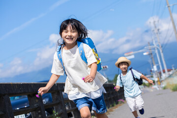 道を走る小学生の女の子と幼稚園児の男の子