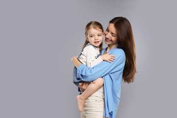Happy mother with her cute little daughter on grey background, space for text