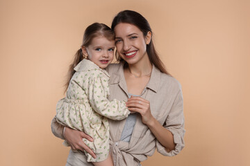 Portrait of happy mother with her cute little daughter on beige background