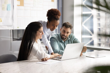 Young African female business leader woman giving consultation to Latin colleagues at laptop,...