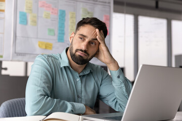 Thoughtful tired Hispanic businessman in casual thinking on project solutions, doubts at laptop,...