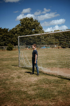 A boy stands in front of a football goal. Goalkeeper