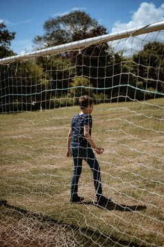 A boy stands in front of a football goal. A view through the net