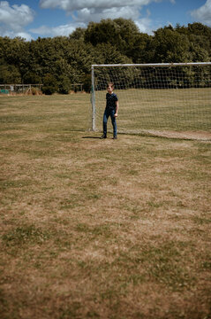 A boy stands in front of a football goal. Goalkeeper