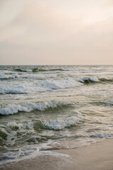 Waves crash on a sandy beach under a soft, hazy sky