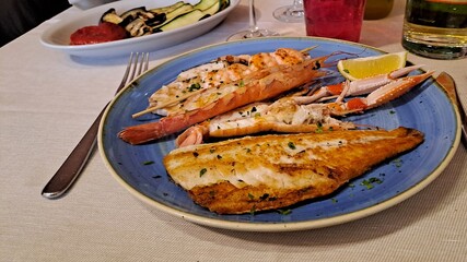 Grilled fish and vegetables with focus on foreground of gourmet dish in Italy.