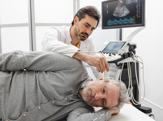Sonographer examines brain of elderly man by placing ultrasound transducer on temple of patient's...