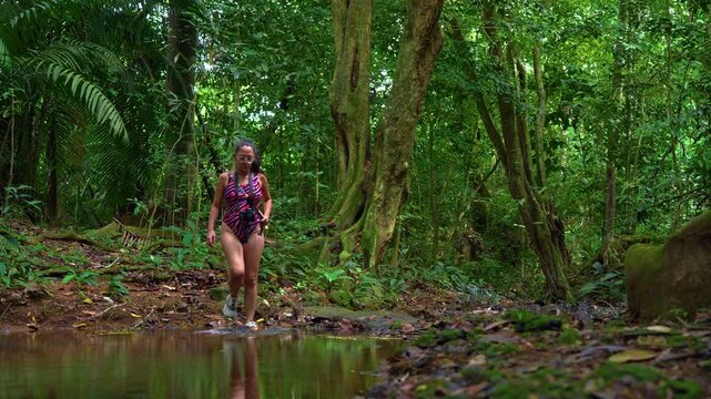 slow motion shot of a young woman crossing a jungle creek in swimwear in Caimito