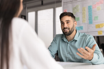 Fototapeta premium Positive young Latin business professional man talking to employer on job interview. Businessman speaking to partner at meeting table, discussing collaboration, partnership