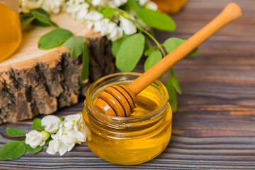 Sweet honey jar surrounded spring acacia blossoms. Honey flows from a spoon in a jar. jars of clear fresh acacia honey on wooden background