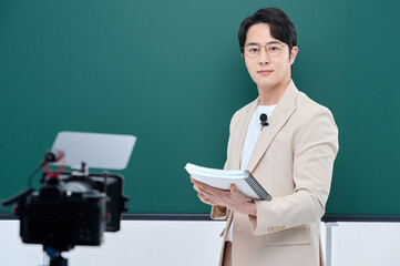 A young male instructor in a suit is holding a book and delivering an online lecture in front of the camera.