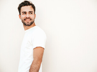 Fototapeta premium Portrait of handsome confident stylish hipster lambersexual model.Man dressed in white T-shirt. Fashion male posing on the street background near wall outdoors