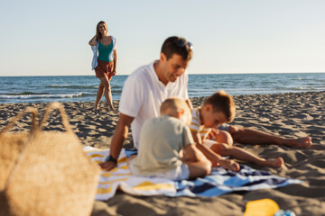 Happy family enjoying beach vacations at sunset, father playing with children while mother walking on seashore