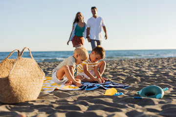 Children playing on the beach while parents walk in the background