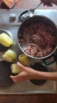 woman preparing food in a kitchen, filling capsicum shell with mince meat, making Croatian food stuffed capsicum
