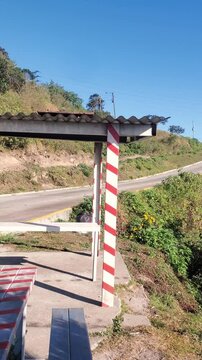 Outdoor shelter with a table and benches, striped poles, Colonia Tovar road background. Sunny day with vegetation