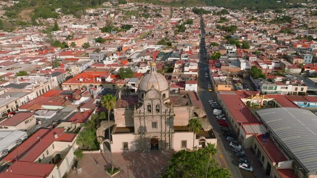 Parroquia del Sagrario and Ciudad Guzm&aacute;n Cathedral, Jalisco, Mexico. Backward drone flight over colonial church with dome and plaza, surrounded by dense urban grid