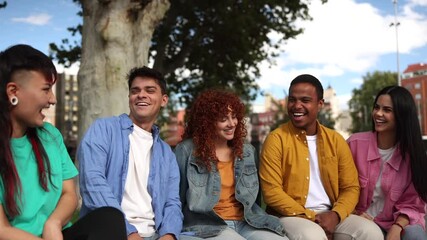Diverse group of young adults sitting on park bench, sharing cheerful conversation and genuine laughter while enjoying urban outdoor leisure moment together - Powered by Adobe