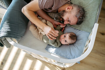 Father putting the baby to sleep, lying next to him in the crib.