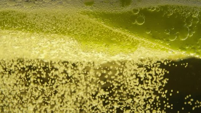 Extreme closeup of fizzy cider surface with apple slice and detailed golden bubbles