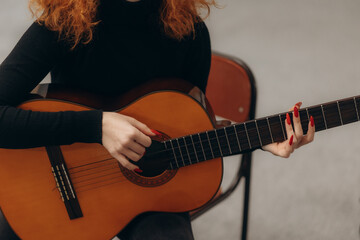 Obraz premium Woman Playing Acoustic Guitar With Red Nails in Relaxed Setting