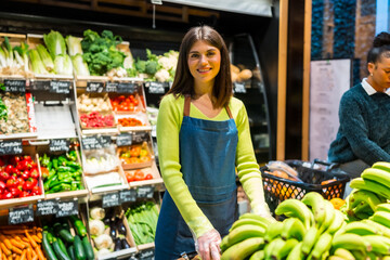 Smiling saleswoman arranging bananas in organic supermarket