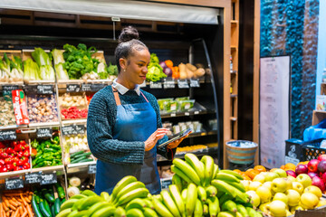 Saleswoman using digital tablet and managing organic food in supermarket