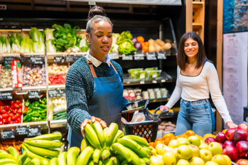 Saleswoman arranging bananas with customer and using digital tablet in organic supermarket