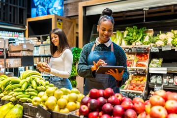 Saleswoman using digital tablet and managing organic products in supermarket