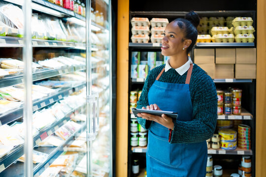 Saleswoman using digital tablet checking food products in refrigerator at organic supermarket