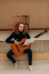 Young Woman Practicing Guitar Music While Reading Sheet Music Indoors