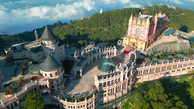Aerial view of the Ba Na Hills featuring a fairytale palace with castles surrounded by lush greenery and clouds.