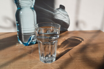Mineral water blue plastic bottle in glass, with sunlight deep shadow of glass. Hard sunlight.