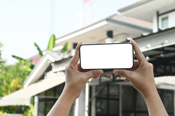 woman's hand holding using smart phone with white blank screen POV at on the background of a house