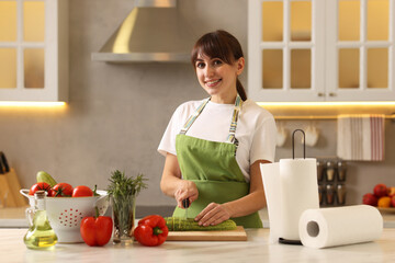 Woman cutting zucchini at white marble table with rolls of paper towels in kitchen