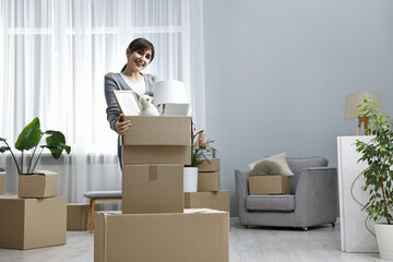 Fototapeta premium Moving day. Happy woman with her belongings in new home, space for text