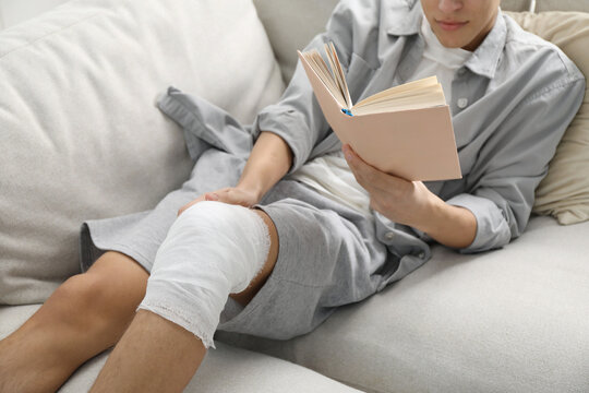 Man with medical bandage on his knee reading at home, closeup - Powered by Adobe