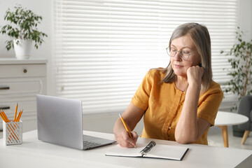 Woman learning online using laptop and taking notes at table indoors. Self-study