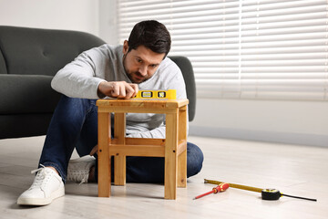 Man using level tool while repairing wooden stool at home