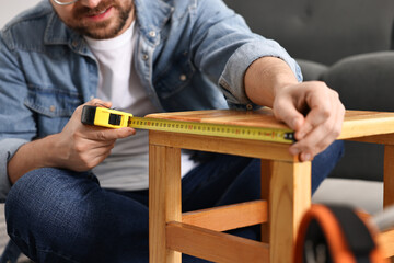 Man using tape measure while repairing wooden stool at home, closeup